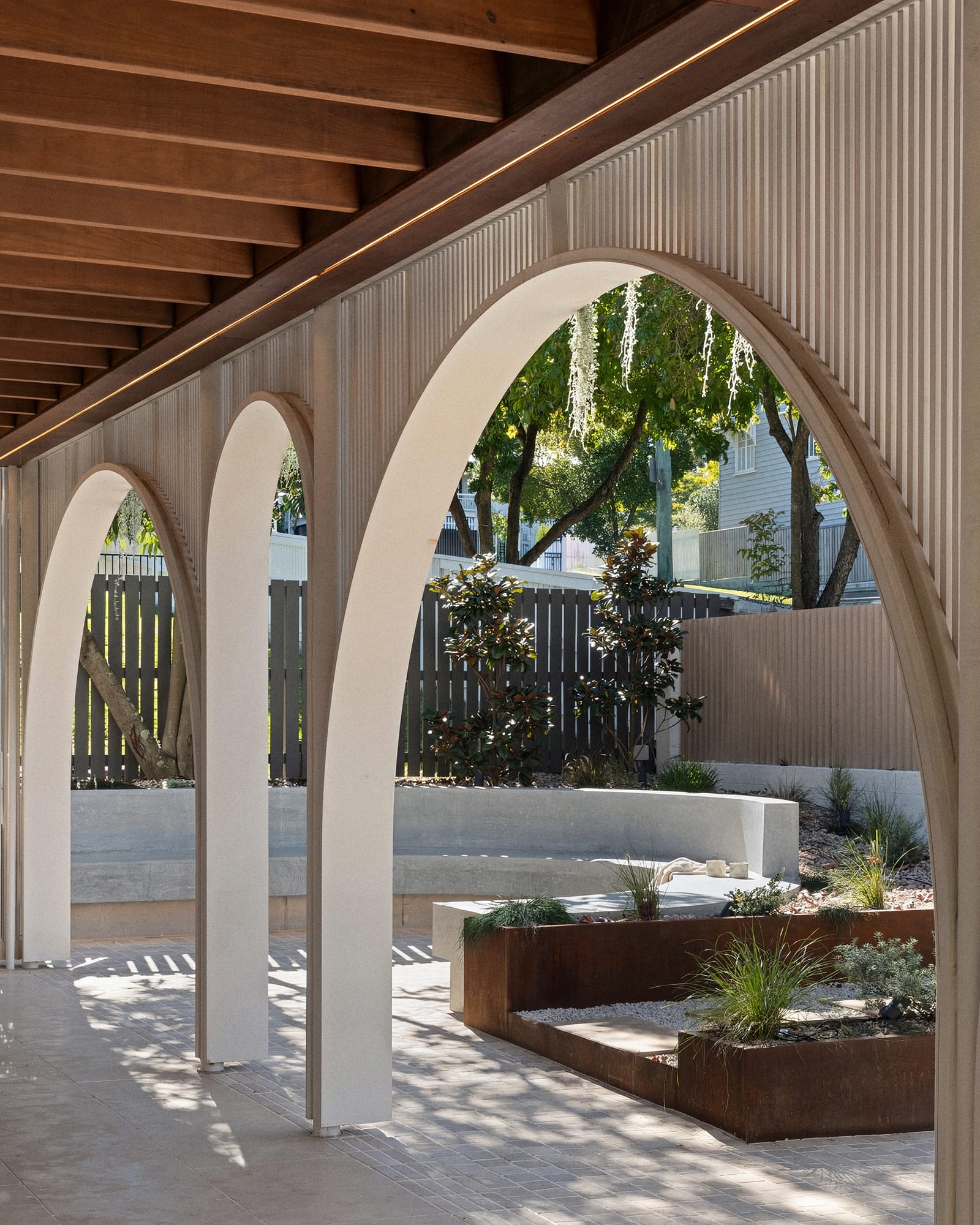 A curved concrete bench beneath white arches, by Bespoke Concrete Co