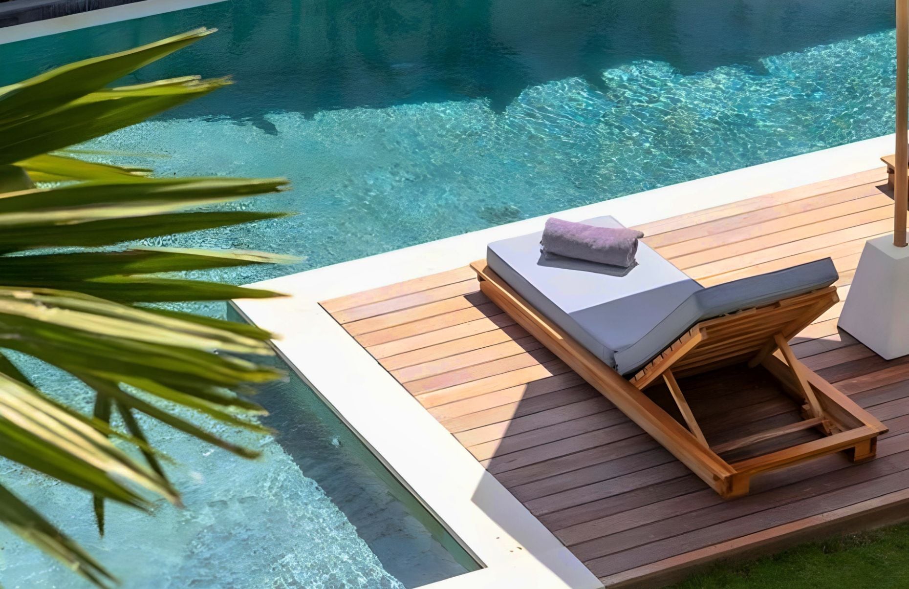 A timber pool deck with a sun lounge beside clear blue water